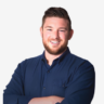 Ben Huizinga headshot - man with beard standing with arms crossed smiling at camera in blue button down shirt