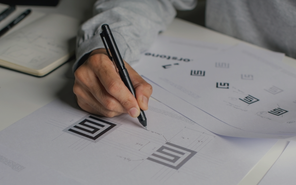 Designers hand holding a pen while working on logo concepts for branding and brand architecture